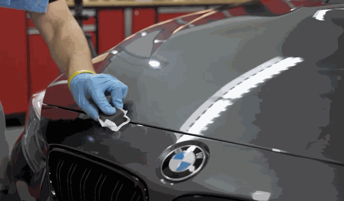 Close-up of a detailer applying ceramic coating to a BMW hood in a Chesterfield, MO garage, creating a glossy protective layer.