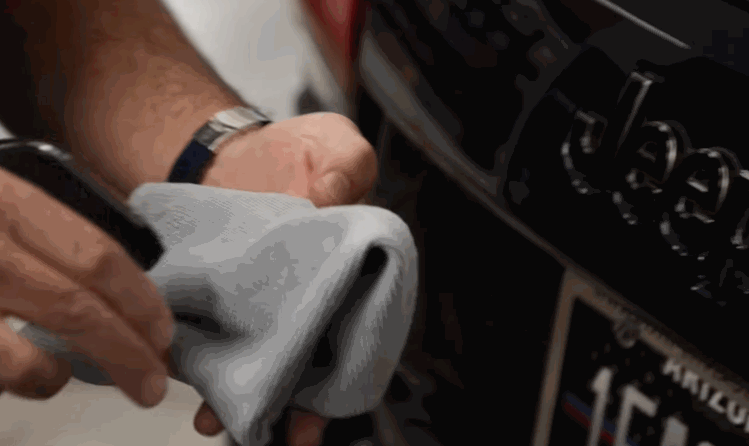 A person sprays ceramic coating onto a gray microfiber towel before applying it to the front of a black Jeep with an Arizona plate.